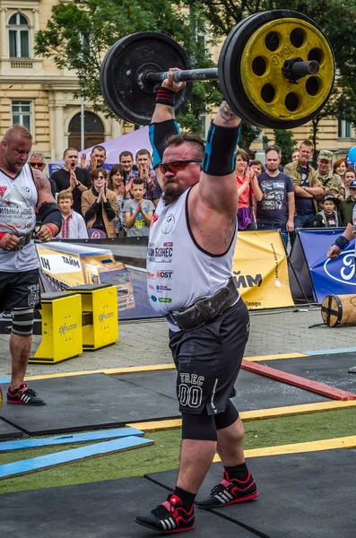 LVIV, UCRANIA - JULIO 2016: Fuerte culturista atleta bombeado hombre fuerte con un cuerpo pesado eleva la barra delante de un grupo de espectadores entusiastas en la calle en un día soleado — Foto de Stock