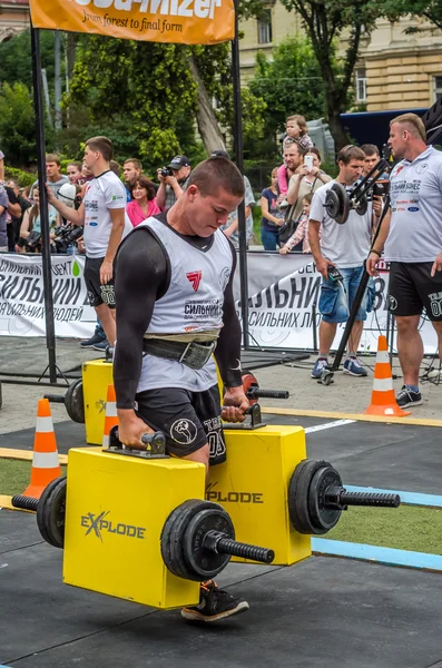 Mighty strong athlete bodybuilder strongman carries heavy iron suitcases on the street in front of enthusiastic spectators