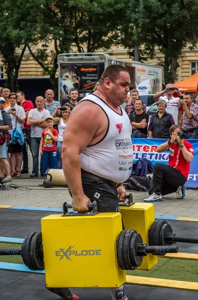 Poderoso atleta fuerte culturista hombre fuerte lleva pesadas maletas de hierro en la calle delante de espectadores entusiastas — Foto de Stock
