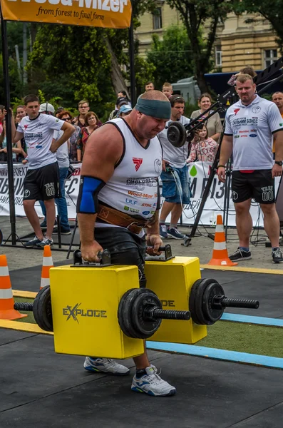 Mighty strong athlete bodybuilder strongman carries heavy iron suitcases on the street in front of enthusiastic spectators