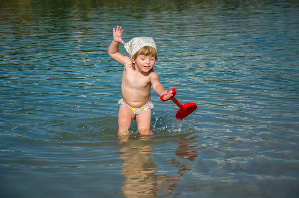 Little charming girl baby playing on the lake swimming in the water during vacation at the resort on a sandy beach — Stock Photo, Image