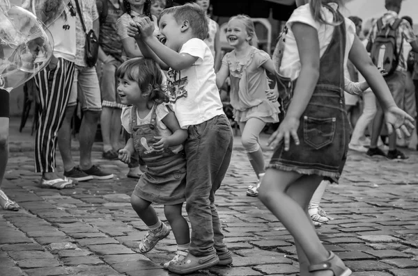 LVIV, UCRANIA - AGOSTO 2016: Niños pequeños atrapando burbujas de jabón en la ciudad, jugando, alegres e irradiando emociones positivas, niños felices — Foto de Stock