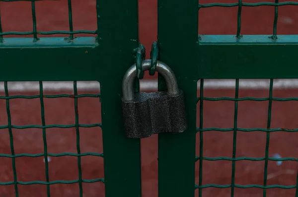 The lock hangs on the gate with a steel fence