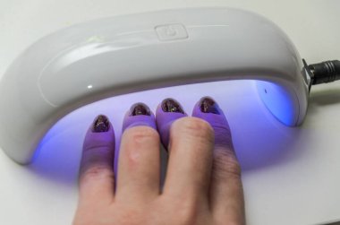 Kadın, manikür üstüne manikür yaparak sertleştirmek için mor ötesi lambayla parlıyor.