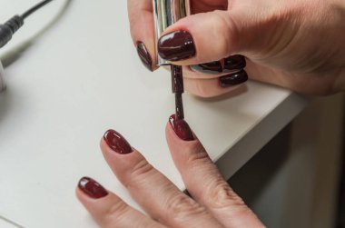 Kadın kendine manikür yapıyor, ojeyle oje sürüyor.