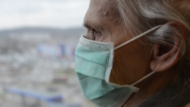 窓の外を見る医療用マスクの高齢女性 — ストック動画