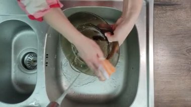 Hizmetçi lavaboda bir tabak yıkar.