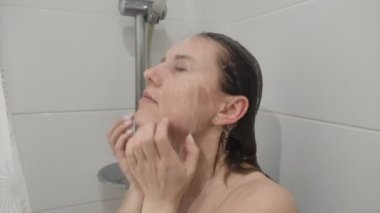 Uzun saçlı, genç ve çekici bir kadın duş alırken başını şampuanla yıkıyor.