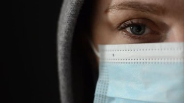 Siyah arka planda izole edilmiş kapüşonlu, tıbbi koruyucu maskeli, spor ceketli genç bir kadının yarı yüzü.