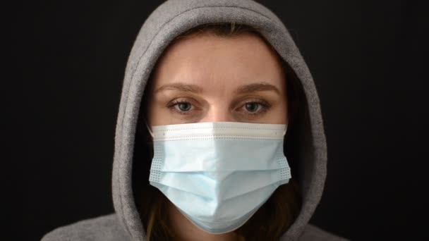 フード付きスポーツジャケットの若い女性は 顔から医療保護マスクを脱いで 黒の背景に隔離された — ストック動画