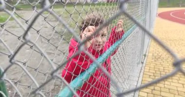 Küçük sevimli kız çocuk oyun bahçesinde çitin arkasında duruyor.