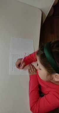 Dikey video. Küçük kız ödev yapıyor, mektup yazmayı öğreniyor.