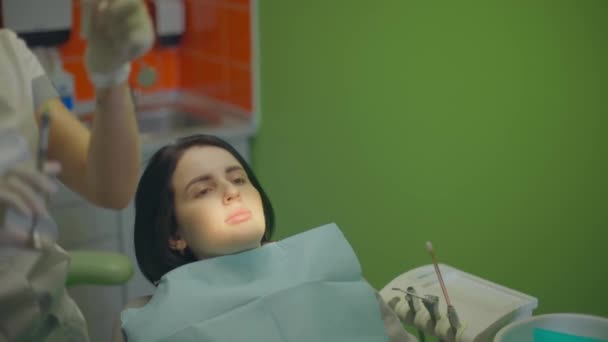 Młoda dama siedzi na fotelu dentystycznym, podczas gdy jej zęby są sprawdzane przez ortodontę w klinice. — Wideo stockowe
