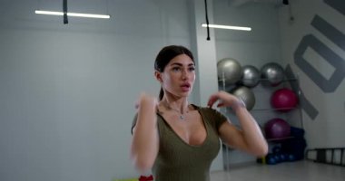 Atletik kadın, modern bir spor salonunda esnekliğini ve gücünü arttırmak için aktif olarak omuz rotasyonlarına katılıyor. Alan çeşitli çalışma ekipmanlarına sahiptir..