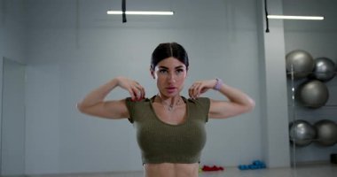 Atletik kadın vücuduna odaklanan omuz rotasyonlarıyla meşgul. Parlak spor salonunda egzersiz ekipmanları ve aynalar var. Egzersiz için enerjik bir atmosfer sağlıyor..