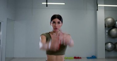 Atletik kadın egzersiz rutininin bir parçası olarak kol daireleri çiziyor. Konferansta gücün ve esnekliğin artırılması üzerinde duruluyor. Parlak ışıklandırma motive edici atmosferi güçlendirir.