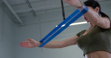 Atletik kadın bir bando çekme egzersizi yapıyor. Dinamik bir egzersiz sırasında direnç bandıyla vücudunun üst kısmını geliştirmeye odaklanıyor..