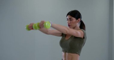 Atletik kadın, spor salonunda halter yükseltirken antrenmanına odaklanıyor. Kararlılığı fitness ve güç eğitimine olan bağlılığını yansıtıyor..
