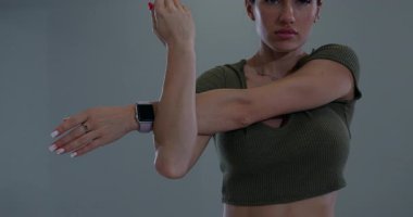 Sporcu bir kadın spor salonunda omzunu esnetiyor. Arka omuz esneme hareketini yaparken şekline odaklanmış görünüyor..