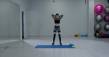 Atletik kadın geniş bir spor salonunda aktif olarak omuz rotasyonu yapıyor. Odaklanmış bir ifadesi var ve antrenman için uygun bir spor kıyafeti giyiyor..
