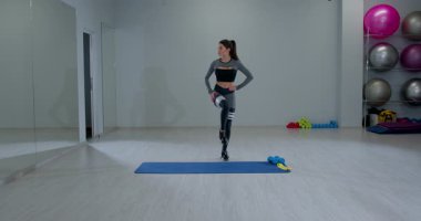 Atletik kadın, parlak bir spor salonunda diz kaldırma egzersizi yapıyor. Çekirdek gücü ve esnekliği üzerinde çalışırken odaklanmayı ve dengesini koruyor..