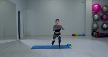 Atletik kadın, iyi aydınlatılmış bir spor salonunda ters atlama egzersizi yapıyor. Etrafı çeşitli spor malzemeleriyle çevrili bir paspasın üzerinde doğru şekli gösteriyor..