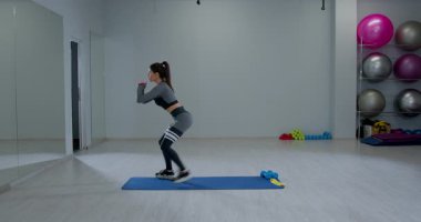 Atletik kadın modern bir stüdyoda spor paspasına ters hamle egzersizi yapıyor. Odaklanmış ve formda. Gücünü ve uygunluğunu gösteriyor..