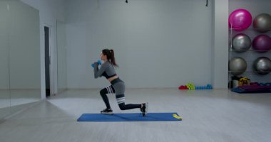 Atletik kadın, iyi donanımlı bir spor salonunda dambıllarla ters hamleler yapmaya odaklanmış durumda. Egzersiz alanında formda kalarak gücünü ve dengesini geliştiriyor..