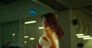 Genç bir kadın şık bir spor salonunda koşu bandında koşuyor. O, antrenmanına odaklanırken onun gevşek saçları arkasından akar. Yumuşak ışık, enerjik atmosferi güçlendirir..