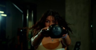 Genç bir kadın kettlebell salıncağını gösteriyor. Bu dinamik egzersizi yaparken saçları gevşek bir şekilde akıyor. Forma olan bağlılığını gösteriyor..