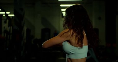 Saçları dökülmüş genç bir kadın omuz gerdirme hareketi yapıyor. Işıklandırma, esnekliği ve gücü üzerinde çalışırken odaklanmış bir atmosfer yaratır..