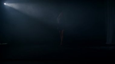 Sarışın kadın, etrafını saran karanlığın içinden geçen bir ışık demetine güvenle yürür. Sahne, tanımlanmamış bir uzayda gizem ve entrikayla dolu bir anı yakalar..