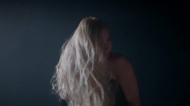 Sarışın kadın dalgalı saçlarını kıvrımlı dumanların arasında nazikçe yeniden düzenliyor zarafetini yansıtan çarpıcı sanatsal bir sahne yaratıyor..