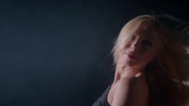 Sarışın kadın kendine güvenen pozunu verirken saçlarını şakacı bir şekilde düzeltiyor. Atmosfer, canlı ve heyecan verici bir gece ortamı olduğunu gösteriyor..