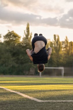 Adam kulaklıklarla futbol sahasında etkileyici bir ters takla atıyor. Güneş onun etrafında güzel bir atmosfer yaratıyor..