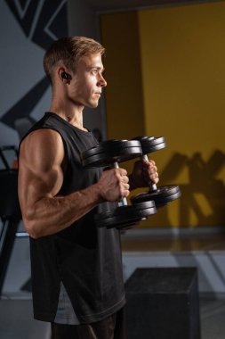 Modern bir spor salonunda elinde iki dambıl olan bir adam çekiç buklelerini düzgün bir şekilde infaz etmeye odaklanıyor. Bu egzersiz kol kaslarını etkili bir şekilde hedef alıyor..