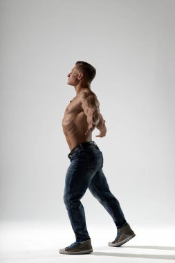 Atletik adam stüdyoda kaslı vücudunu sergiliyor. Forma ve sağlığa olan bağlılığını özgüvenle vurguluyor. Işıklandırma onun formunu vurguluyor..