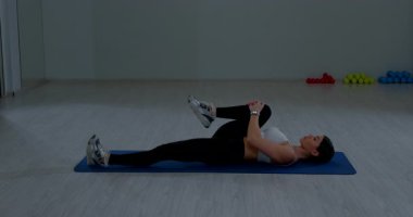 Genç esmer sporcu kadın yoga mat fitness merkezinde bacak esnetiyor.