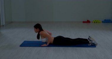 Formda bayan sporcu geniş spor salonundaki paspasın üzerinde sırt gerdirme egzersizi yapıyor.