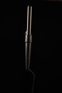 Saç maşası, tasarımı ve yapısını gösteren karanlık bir yüzeye dayanır. Ayarlar saç için kullanılan şekillendirme araçlarını vurgular. Saç bakımında kullanıma hazır..