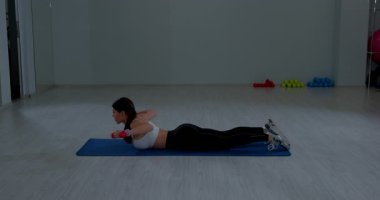 Spor kıyafetleri içinde odaklanmış bir kadın sırt egzersizi için halterleri kaldırıyor.