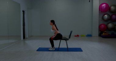 Parlak fitness merkezindeki sandalyeye oturan elastik ilmikli kadın sporcu antrenman bacakları.