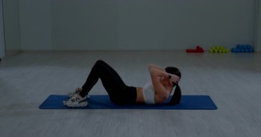 Kadın sporcu, iç mekan egzersizi sırasında yerde mekik çekerek vücut kaslarını güçlendiriyor.