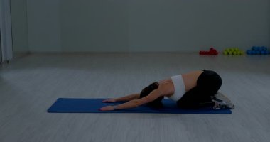 Kadın sporcu, kapalı alandaki yoğun antrenmandan sonra paspasın üzerinde kaslarını gevşetiyor