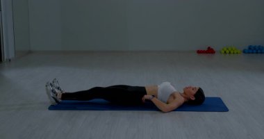 Tozlu ve sırt üstü uzanmış spor elbiseli bir kız. Sağlık kulübünde karın kaslarını çalıştırıyor.