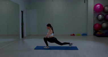 Fit esmer kadın bacaklarını açıyor yoga minderi pozisyonu alıyor spor kulübünün içini eğitiyor.