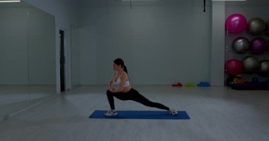 Sporcu kadın, geniş aerobik salonunda antrenmandan önce kaslarını ısıtıyor.