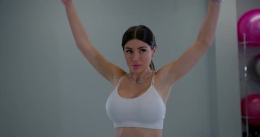 Adanmış sporcu kadın vücudunun üst kısımlarını çalıştırıyor kollarını kapalı spor salonunda yükseğe kaldırıyor.