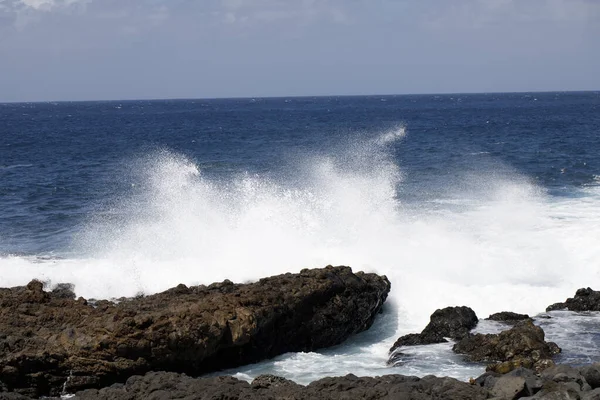 Dalgalar, arka planda ufuk olan Kuzey Atlantik adasının engebeli volkanik kıyısı boyunca uzanan bu kıyı şeridine güçlü bir şekilde çarpar..