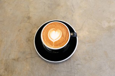 Beton arka planda bir fincan sıcak kapuçino. Kalp şeklinde sanat latte. Aşkın sembolü. Sevgililer Günü konsepti